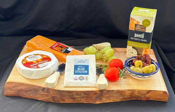 A wooden board displaying various cheeses, grapes, cherry tomatoes, olives, and crackers.