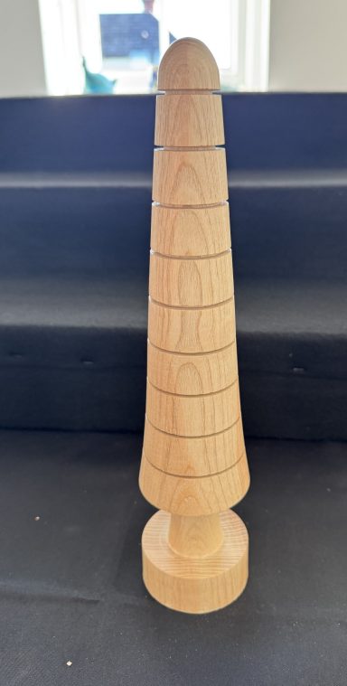 A tall wooden sculpture with a conical shape and engraved lines.