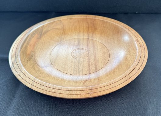 A smooth, polished wooden bowl with circular patterns and a light brown finish.