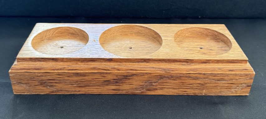 A wooden holder with three circular indentations for candles or small items.