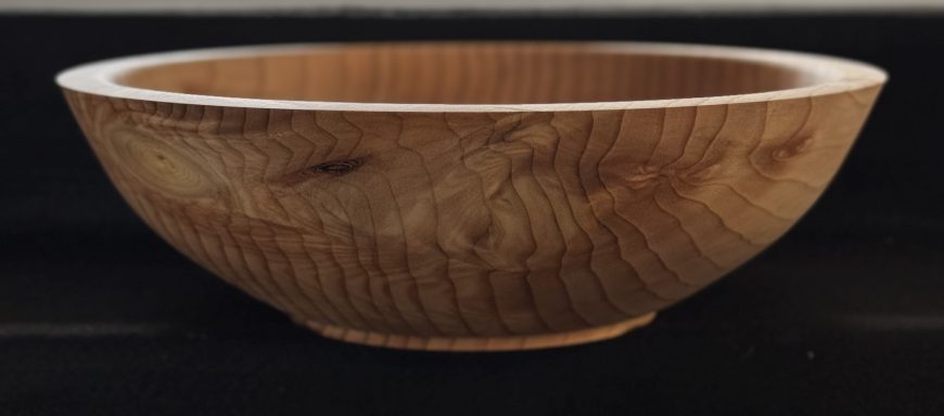 A polished wooden bowl with a smooth, curved design and natural grain patterns.
