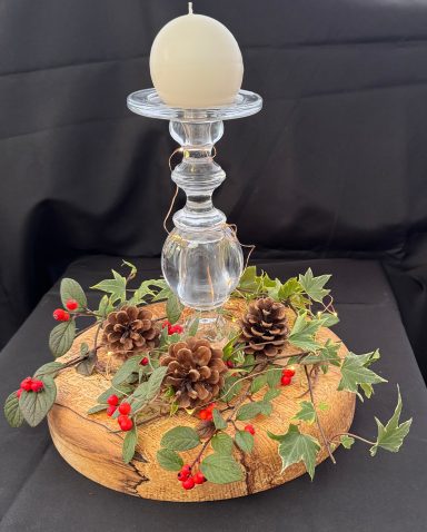 Glass candle holder atop a wooden base with pinecones and red berries.