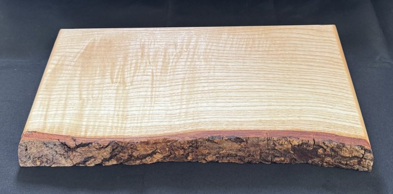 Light wood slab with a smooth surface and rough bark edge.