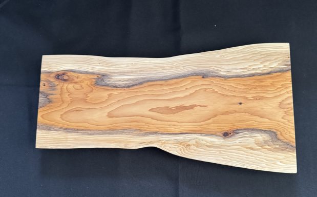 A smooth wooden cutting board with a natural edge and varied brown tones.