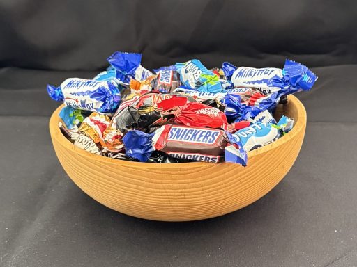A wooden bowl filled with assorted wrapped candies on a dark background.