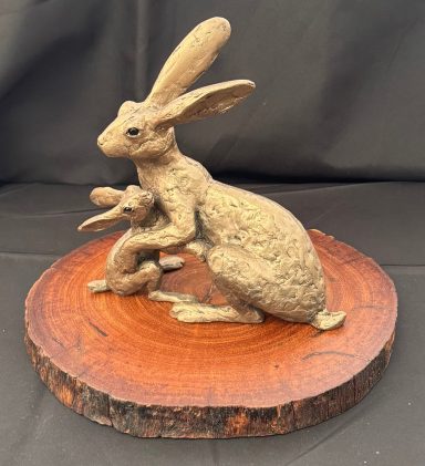 Bronze sculpture of a mother rabbit with her young, mounted on a wooden base.