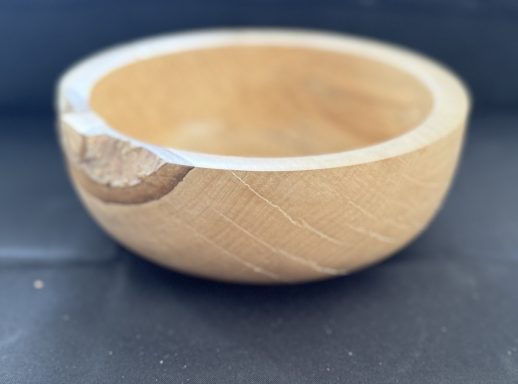 A smooth, round wooden bowl with a natural finish and a small indentation on the rim.