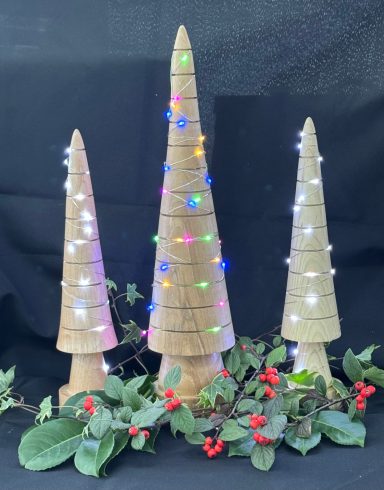 Three conical Christmas trees made of natural materials, decorated with colourful lights and foliage.