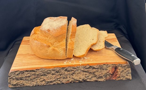 Loaf of sliced bread on a wooden board with a knife beside it.