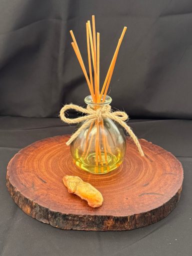 Glass diffuser bottle with reed sticks on a wooden platter, accompanied by a small stone.
