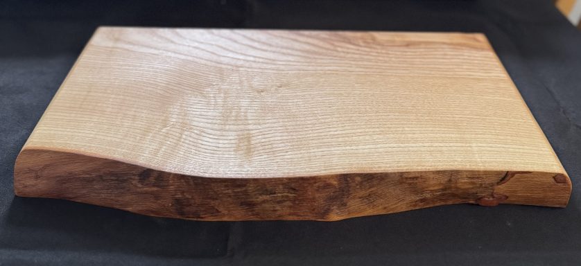 Natural wood serving board with a smooth surface and curved edge.