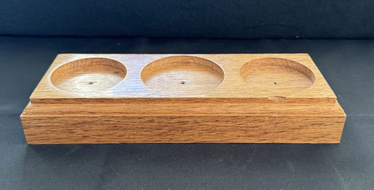 Wooden holder with three circular indentations on a dark background.