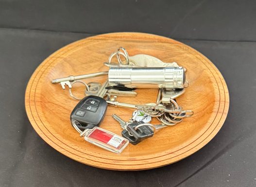 A wooden plate holding a set of keys and a silver keychain device.